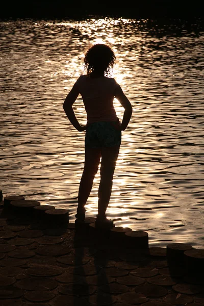 Kobieta sylwetka w pobliżu wody na zachód słońca — Zdjęcie stockowe