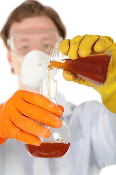 Scientist in respirator and rubber gloves pours brown liquid fr — Stock Photo, Image