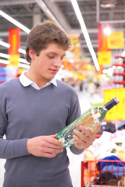 Jovem no supermercado com garrafa de álcool — Fotografia de Stock