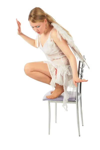 Flicka i ängelns kostym knäböj på stol — Stockfoto