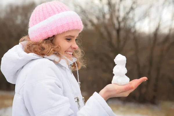 Молодая красотка на открытом воздухе зимой держит в руках маленького снеговика — стоковое фото