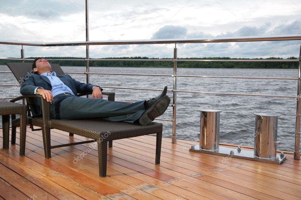Portrait of man, who rests in chaise lounge on wharf near water