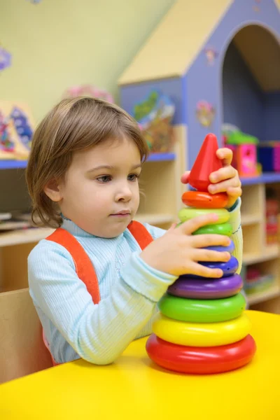 Little girl plays in kindergarten with plastic pyramid — Stock Photo, Image