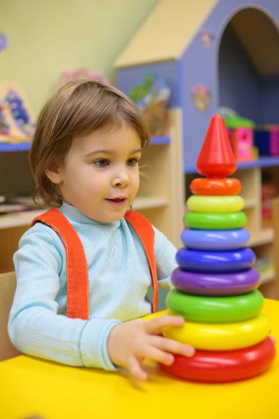 Маленькая девочка играет в детском саду с пластиковой пирамидой — стоковое фото