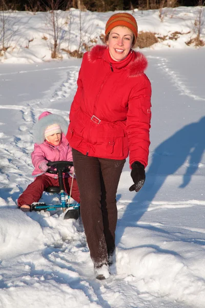 Мать тянет дочь на снежном скутере — стоковое фото