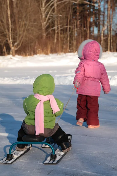 Ребенок тянет другой на снежном скутере со спины — стоковое фото