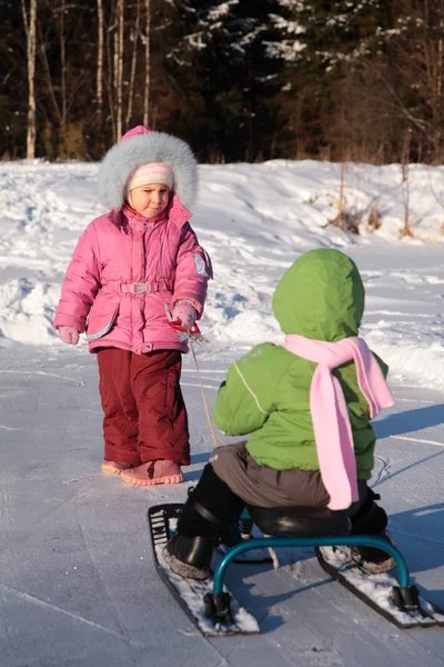 Ребенок тянет другой на снежном скутере — стоковое фото
