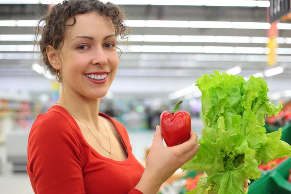 Молодая женщина в магазине с красным сладким перцем и салатом — стоковое фото