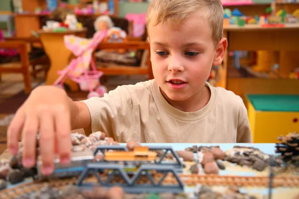 Мальчик играет с игрушечной железной дорогой в игровой комнате — стоковое фото