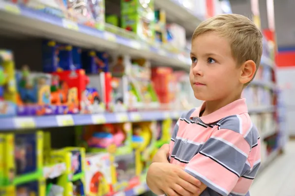 Rapaz olha prateleiras com brinquedos na loja — Fotografia de Stock