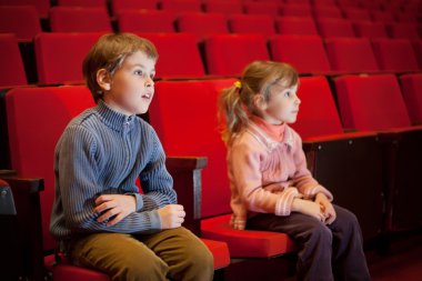 Boy and little girl sitting on armchairs at cinema clipart