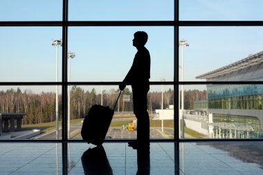 Silhouette of man with luggage standing near window in airport s clipart