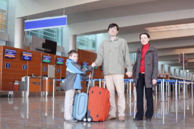 Family with boy standing in airport hall with suitcases full bod clipart