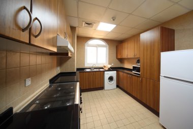 Kitchen with brown cupboards, washingmachine, cooker and fridge clipart