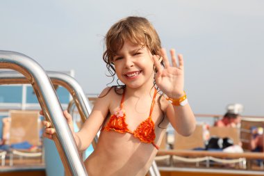 Caucasian little girl standing on cruise ship, smiling and wavin clipart