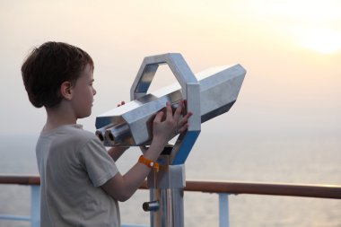 Little boy standing near binocular and looking into the distance clipart