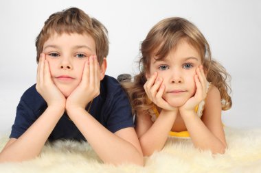 Little boy and girl lying on white fell, chin on hands, looking clipart