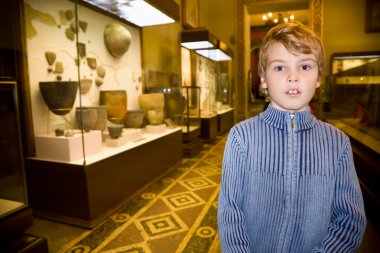 Boy at excursion in historical museum near exhibits of ancient r clipart