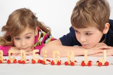 Little boy and girl lying on floor and playing with wooden alpha clipart