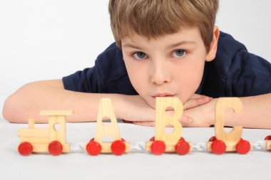 Little boy lying on floor and playing with wooden alphabet railw clipart