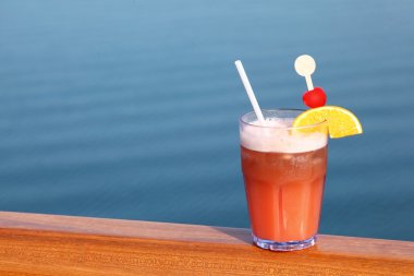 Cocktail with fruits in glass on ship deck rail, sea on backgrou clipart