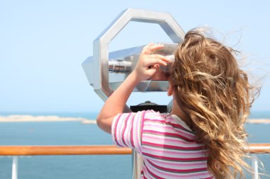 Little girl standing on cruise liner deck and looking in binocul clipart