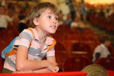 Little boy in circus leans on red rail looking into the distance clipart