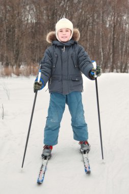 Little boy in warm sport dress skiing at forest, full body, look clipart