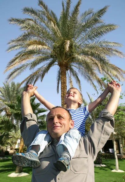Aîné avec enfant sur les épaules devant un collage de palmiers — Photo