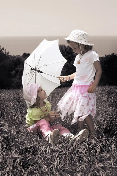 与两个小女孩用一把雨伞在草坪上的老式照片 — 图库照片