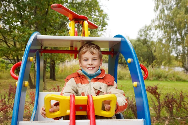 Мальчик в куртке на детской площадке в осеннем парке — стоковое фото