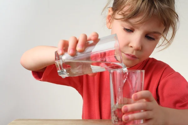 Kleines Mädchen im roten Hemd schüttet Wasser von einem Glas ins andere, — Stockfoto