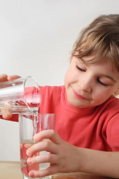 Маленькая девочка в красной рубашке льет воду из одного стакана в другой , — стоковое фото