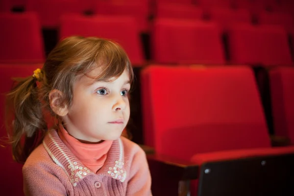 Маленькая девочка сидит на креслах в кинотеатре, непоколебимо глядя — стоковое фото