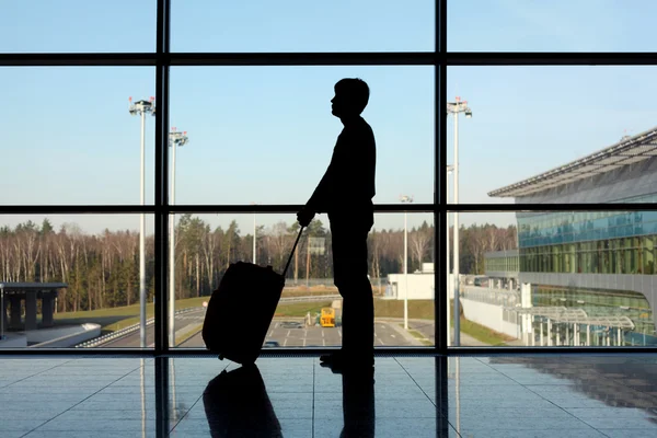 Silhouet van man met bagage staande in de buurt van venster in luchthaven s — Stockfoto