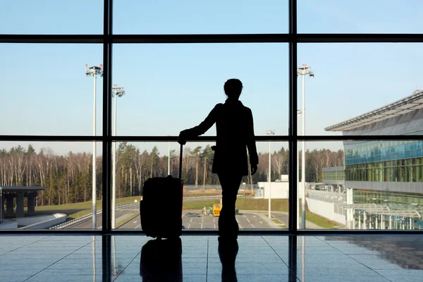 Silhouet van meisje met bagage staande in de buurt van venster in luchthaven — Stockfoto