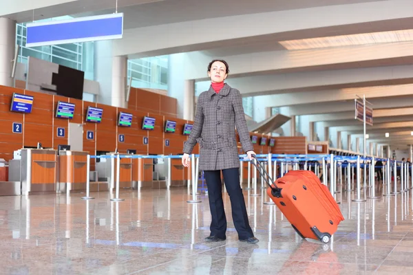 Chica con maleta roja de pie en la sala del aeropuerto — Foto de Stock