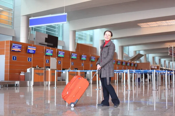 Chica con maleta roja de pie en la sala del aeropuerto vista lateral — Foto de Stock