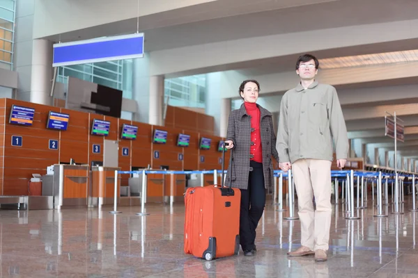 Man and girl with red suitcase standing in airport hall looking — Stock Photo, Image