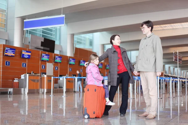Young family with red suitcase standing in airport hall — Stock Photo, Image