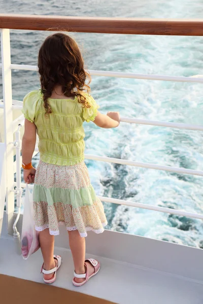 Маленькая кудрявая девочка стоит на палубе корабля и смотрит на волны — стоковое фото