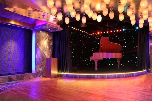 Grand piano op het lege podium met houten vloer en veel decor lamp — Stockfoto
