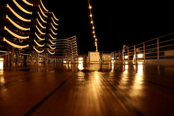 Deck de navio de cruzeiro vazio com cadeiras de praia e lâmpadas à noite — Fotografia de Stock
