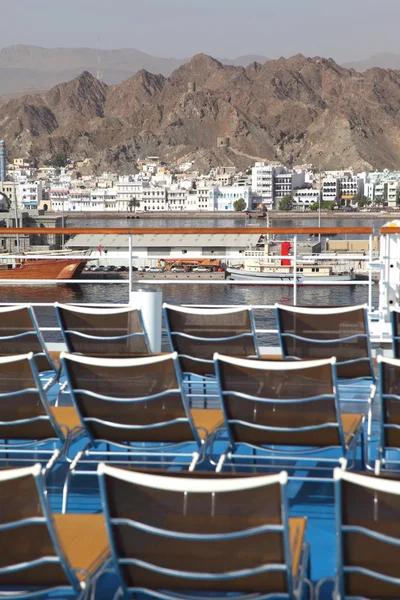 Cadeiras de praia marrom no convés do navio azul no porto perto de montanhas — Fotografia de Stock