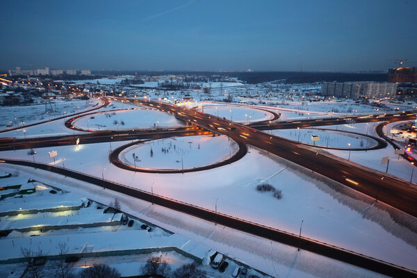 Evening winter cityscape with big interchange, lighting columns and garages