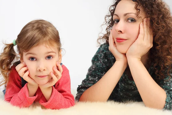Klein meisje en haar moeder ligt op witte fell, handen op kin, loo — Stockfoto
