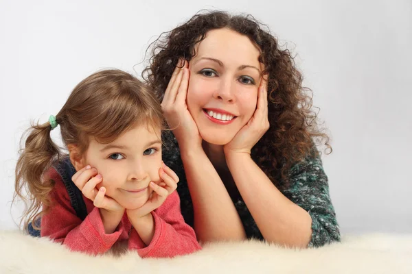 Little girl and her mother with toothy smile lies on white fell, — Stock Photo, Image