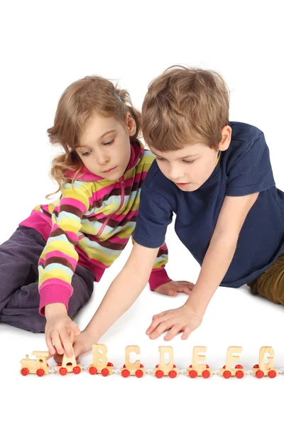 Little boy and girl playing with wooden railway sitting on floor — Stock Photo, Image