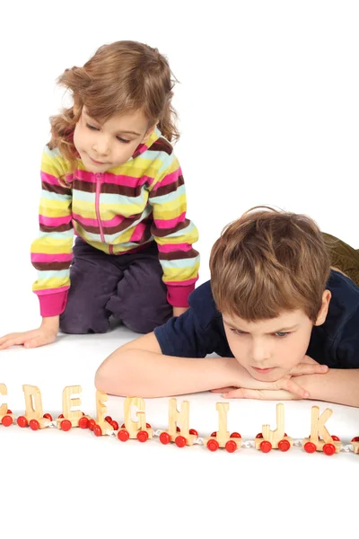 Маленькие серьезные мальчик и девочка играют с деревянной железной дорогой, фокус — стоковое фото