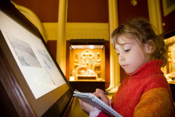 Маленькая девочка, стоящая рядом с монитором, пишет книги на exc — стоковое фото